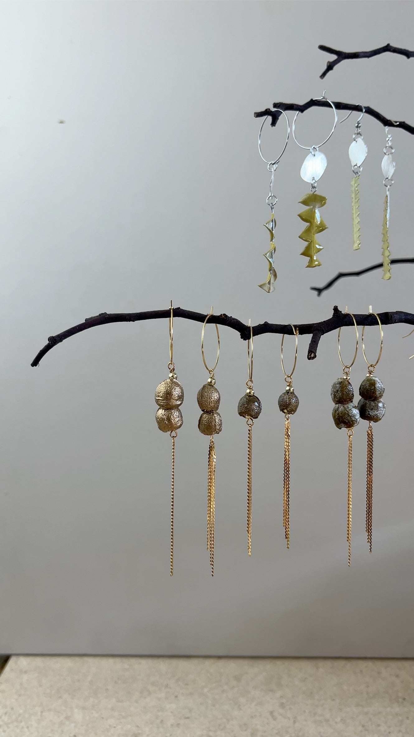 Set of earrings hanging from a branch against a plain background