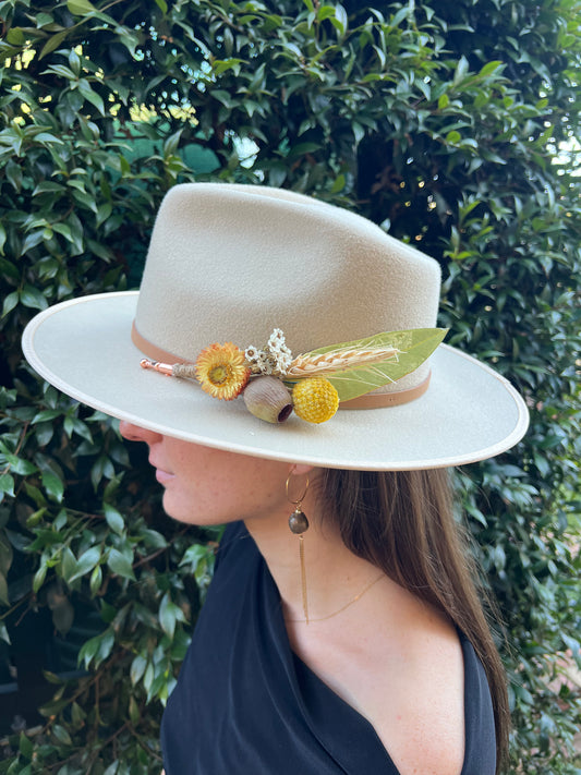 Woman wearing a white hat with decorative elements against a green leafy background