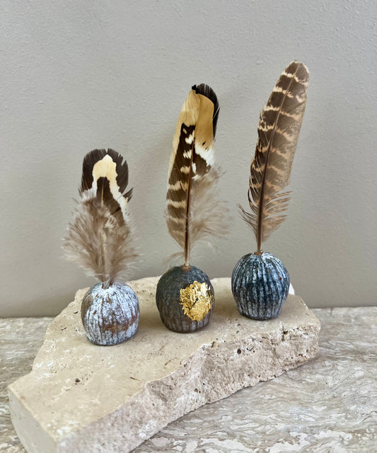 Decorative gumnut feather desk items with feathers on spherical bases on a stone surface.