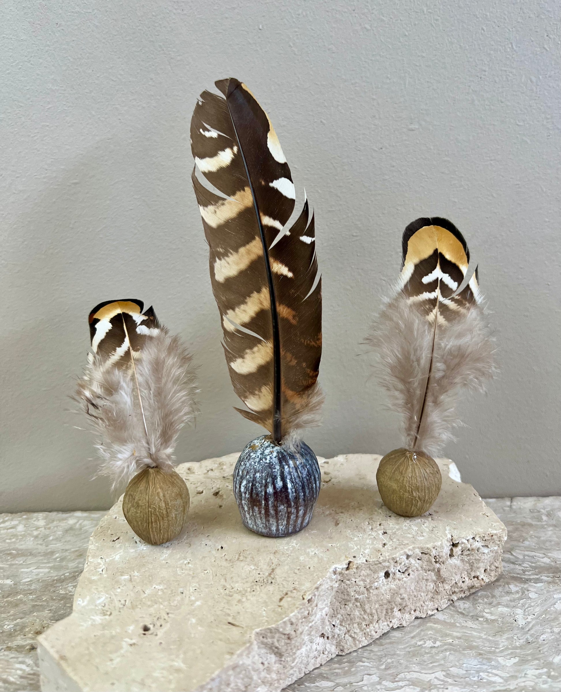 Decorative arrangement with feathers and small balls on a stone base against a plain background