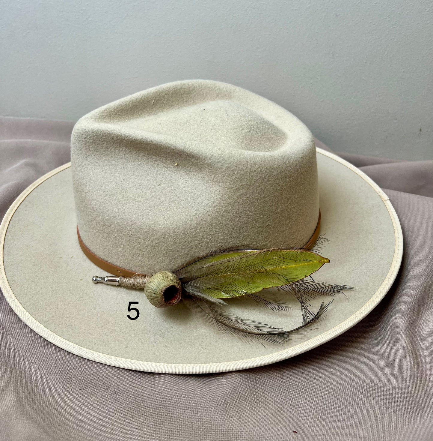 Beige hat with feather detail on a gray fabric background