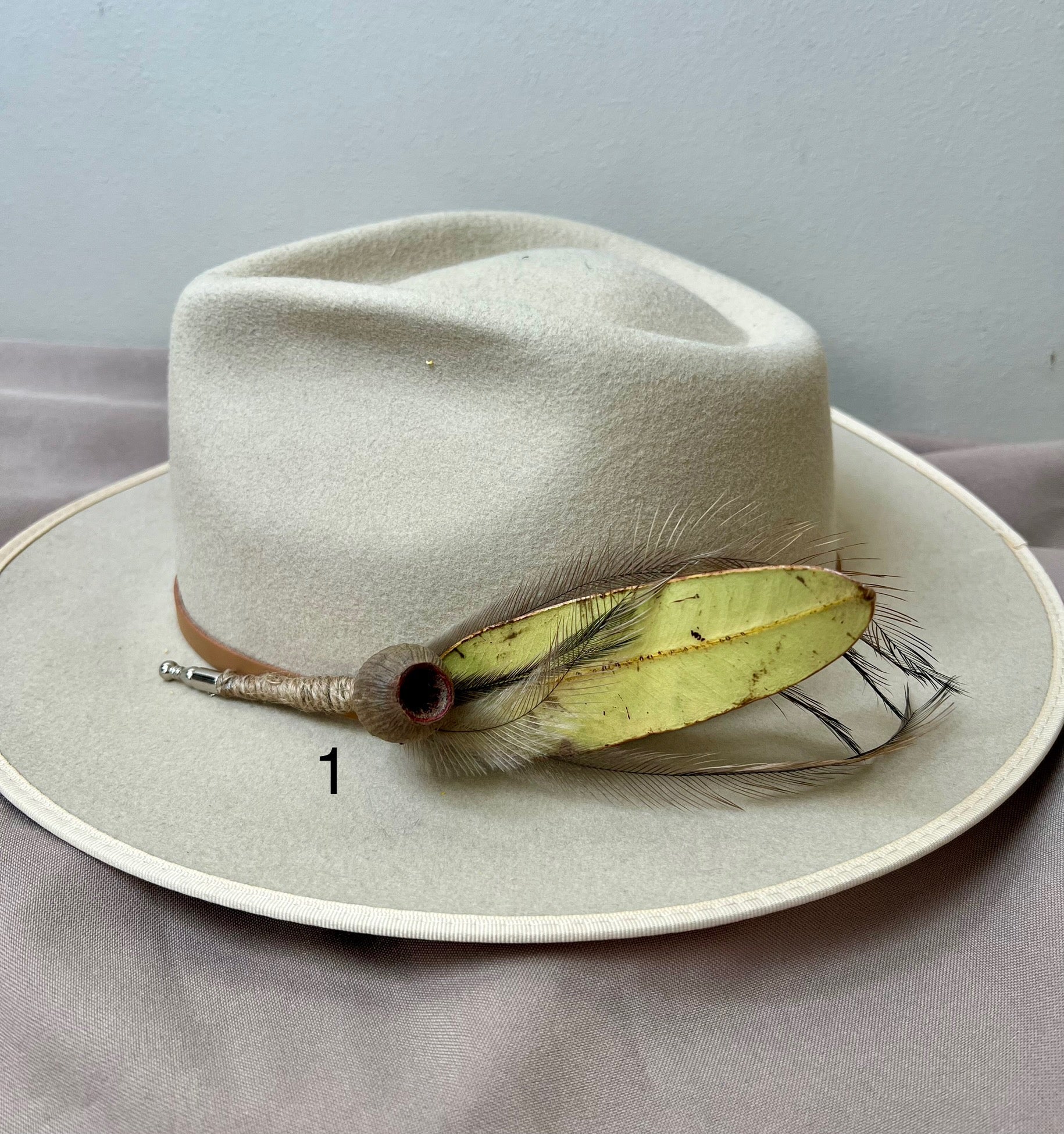 White fedora hat with a feather detail on a gray surface