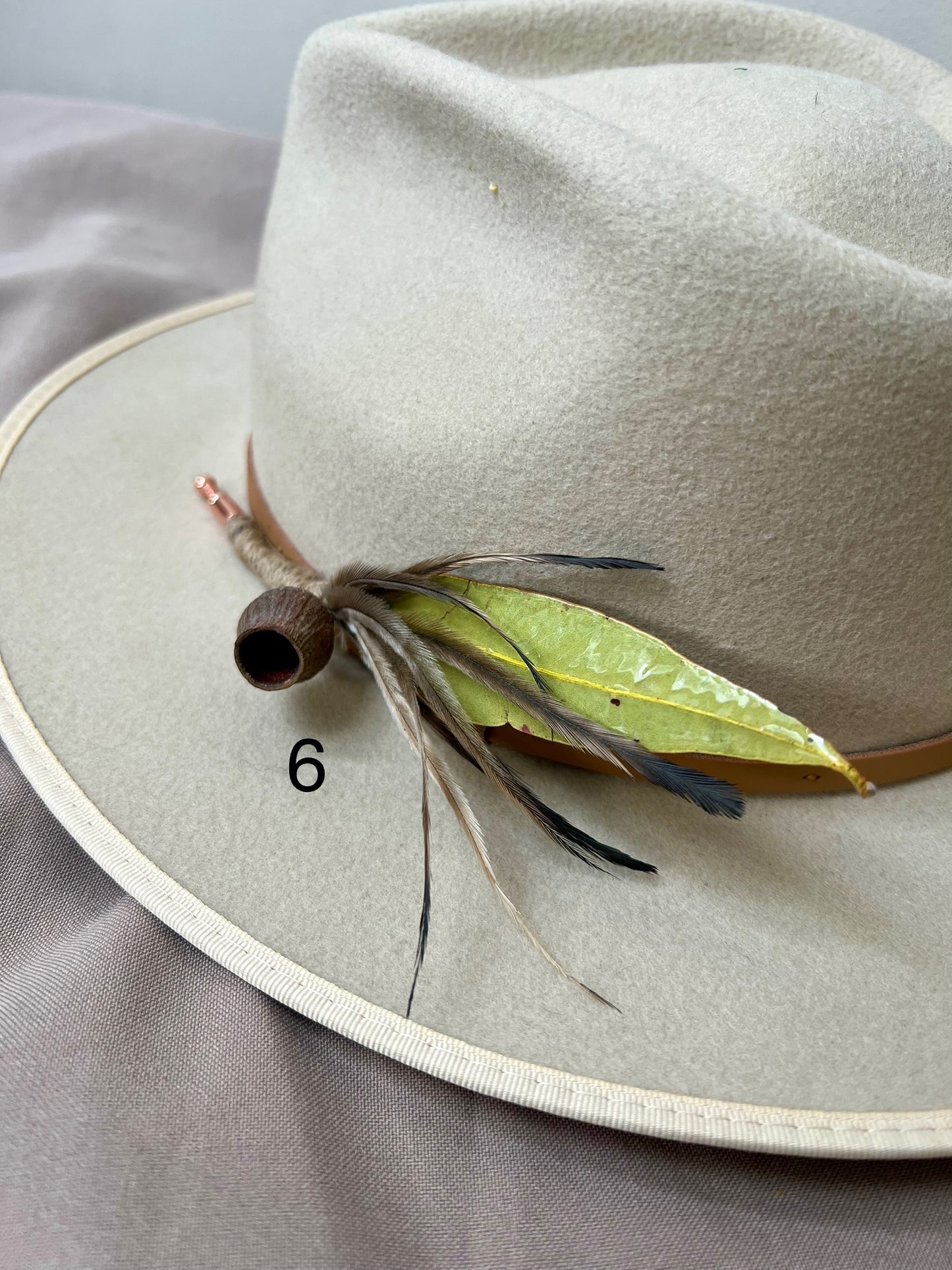 Beige hat with feather and leaf decoration on a gray background