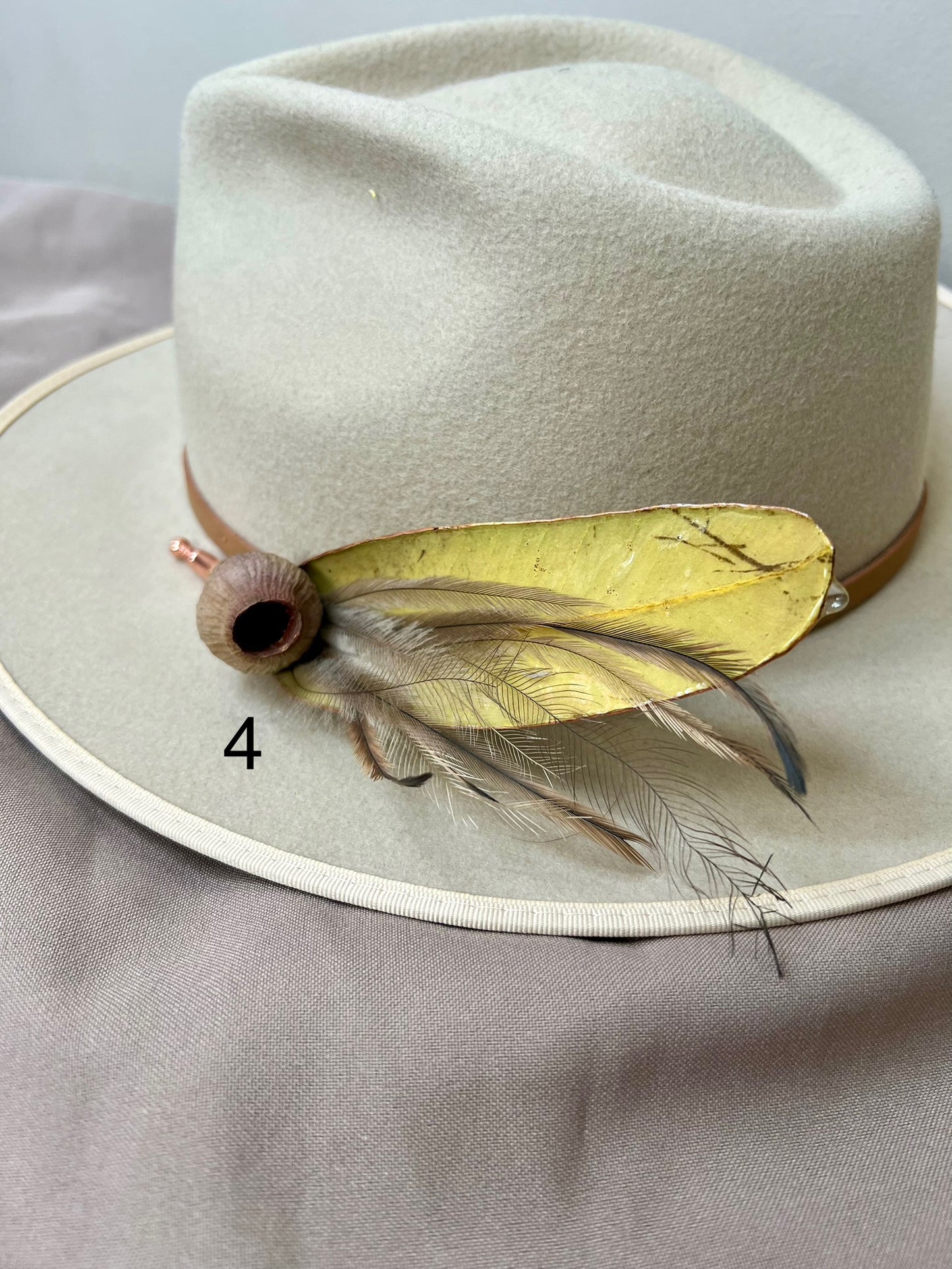Beige hat with a decorative feather and ribbon on a gray background