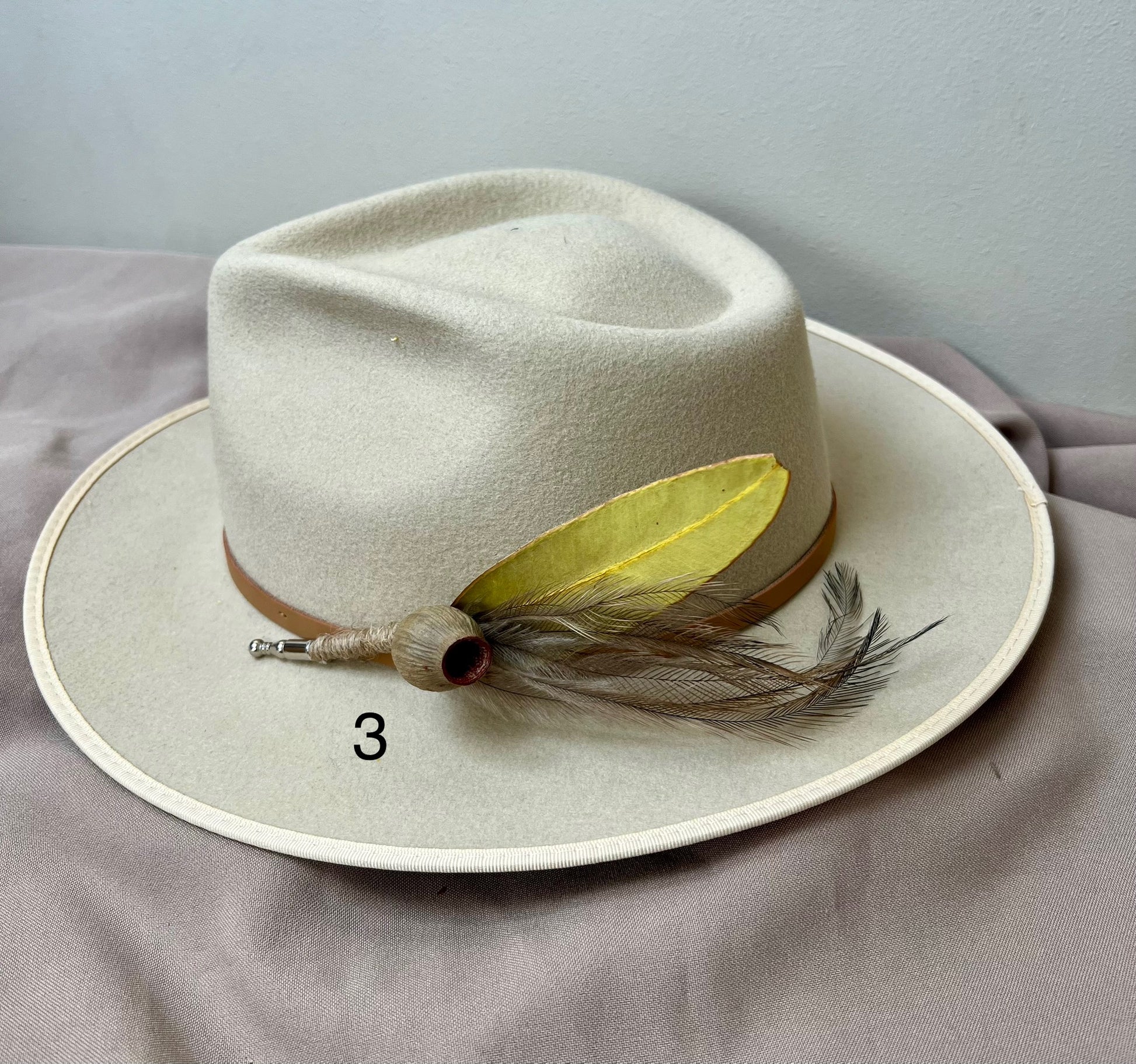 White fedora hat with a yellow feather on a gray surface
